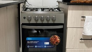Une cuisine équipée d’une nouvelle cuisinière à gaz de grande capacité (62 litres), d’une bouilloire et d’une bouteille d’eau posées sur le plan de travail.