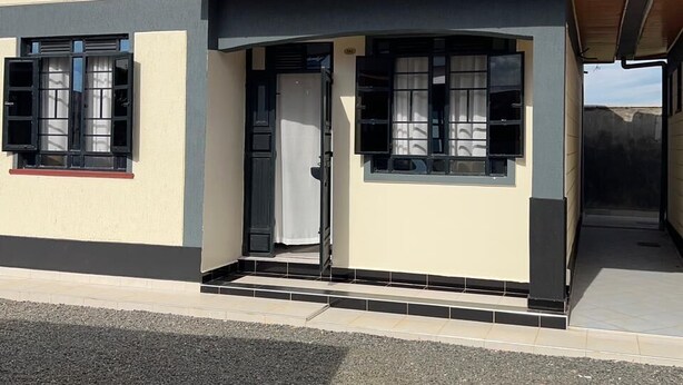 Une maison de plain-pied avec un toit recouvert de tuiles rouges, une façade beige et un petit porche à l’avant.