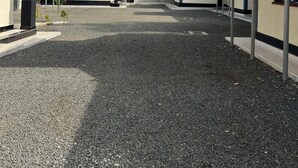 Un bâtiment avec une allée en gravier et des places de stationnement couvertes.