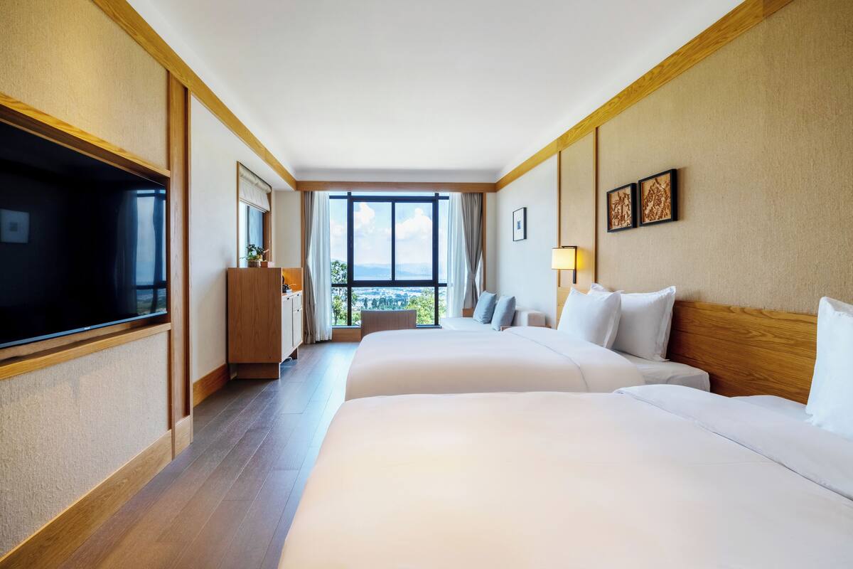 Habitación de hotel con dos camas, televisión, escritorio y una ventana grande con vistas.