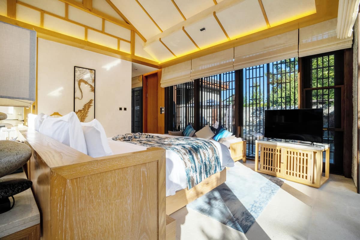 Un dormitorio con cama, televisor, una consola de madera y ventana con vistas.