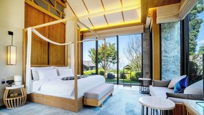 Un dormitorio amplio con cama con dosel, una zona de estar con sofá y mesa de centro, y vistas al exterior.