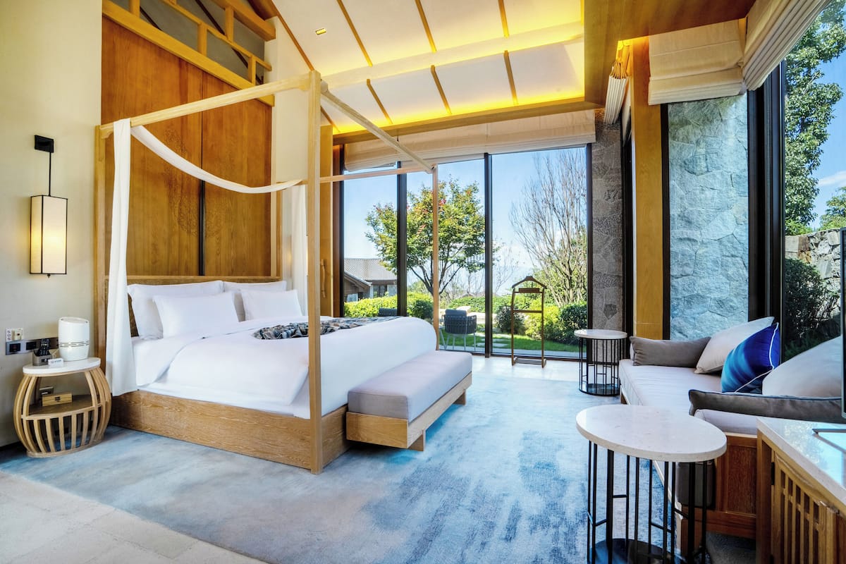 Un dormitorio amplio con cama con dosel, una zona de estar con sofá y mesa de centro, y vistas al exterior.