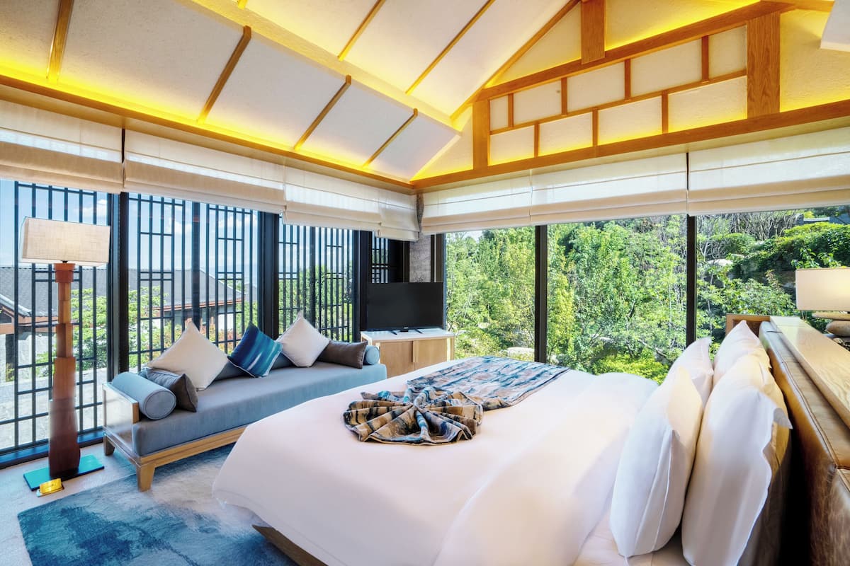 Un dormitorio con una cama grande, un sofá, un televisor y vistas a zonas verdes.