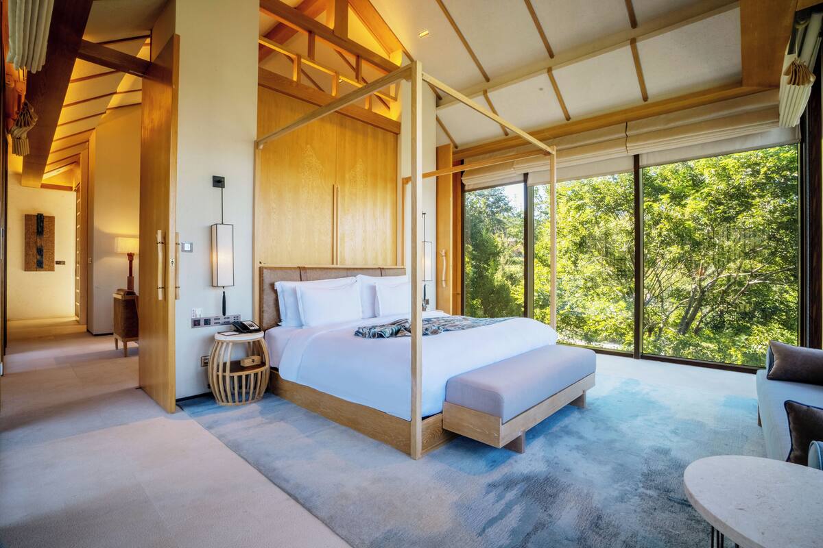Un dormitorio amplio con una cama grande, una mesita de noche, una silla y vistas al exterior.