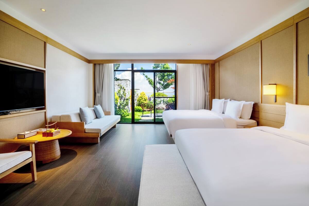 Habitación de hotel con una cama grande, un sofá, un televisor y vistas a zonas verdes.