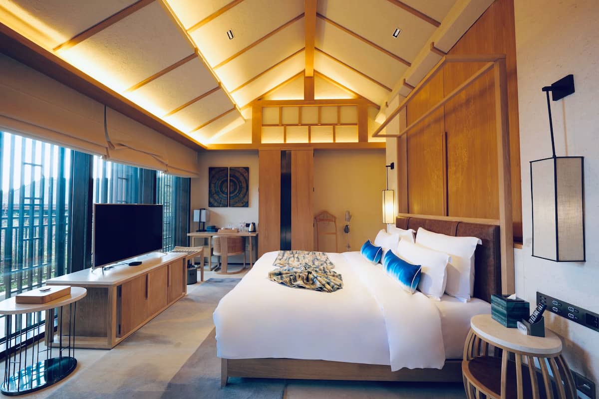 Una habitación de hotel moderna con una cama grande, un escritorio, un televisor y un balcón con ventanas amplias.