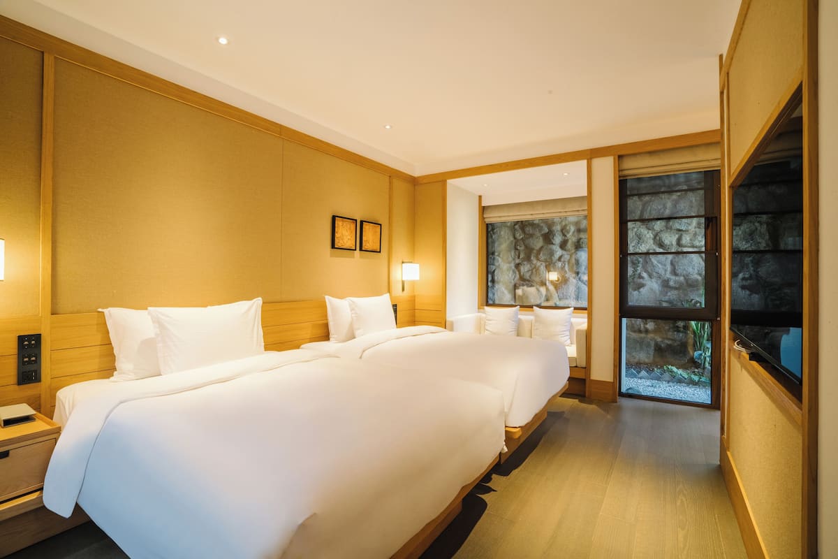 Habitación de hotel con una cama grande, mesitas de noche, una ventana con vistas a un paisaje rocoso y un televisor montado en la pared.