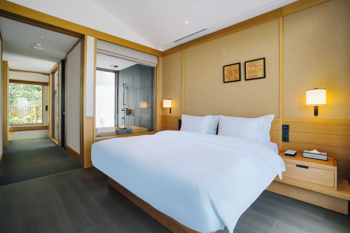 Habitación de hotel con una cama grande, mesitas de noche, un espejo y una puerta que da a un baño.