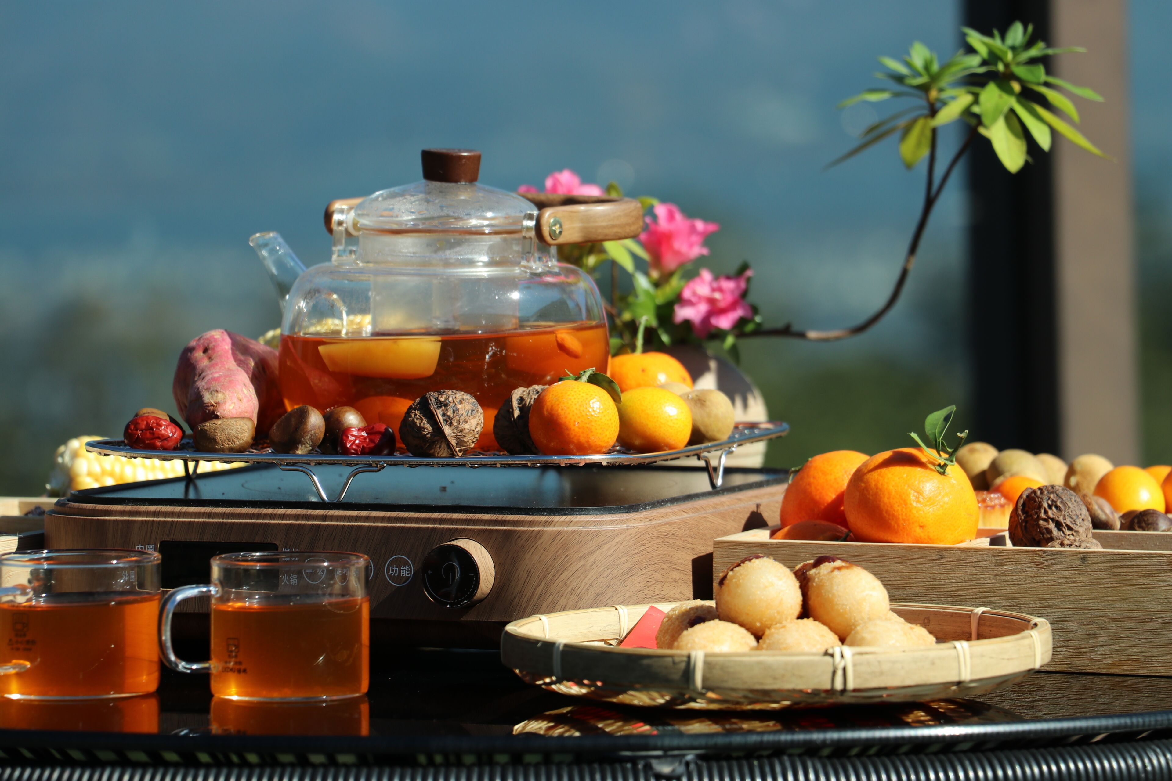 A tea set with teapots and cups, a tray with oranges and nuts, and a wicker table.