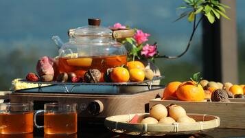 A tea set with teapots and cups, a tray with oranges and nuts, and a wicker table.