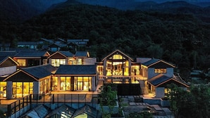 Una casa grande y moderna con varios niveles y amplias ventanas, rodeada de un paisaje montañoso.