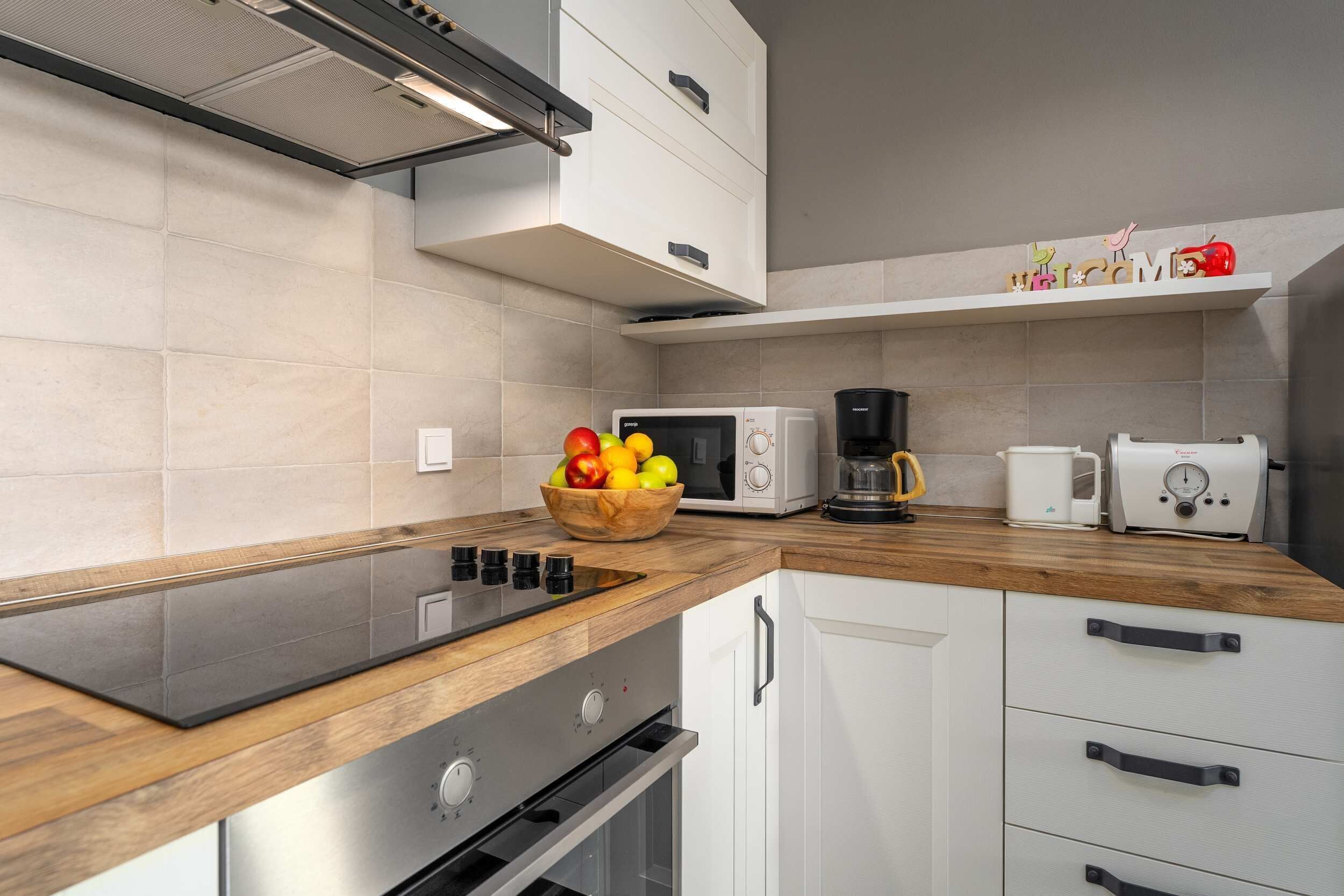 Een moderne keuken met een houten aanrecht, een ingebouwde oven, een magnetron en een koffiezetapparaat.
