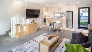 Eine moderne Wohnung mit Wohnzimmer, Essbereich, Küche und einem an der Wand befestigten Fernseher.