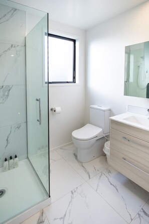 Een moderne badkamer met een douchecabine van glas, een toilet, een wastafel met spiegel en marmeren vloeren.