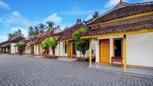 A row of traditional buildings with tiled roofs, a paved courtyard, and palm trees. - OYO 95262 Hotel Djatmiko Villa's Family  (Sumberagung)
