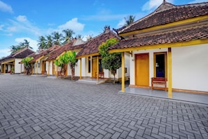 A row of traditional buildings with tiled roofs, a paved courtyard, and palm trees. - OYO 95262 Hotel Djatmiko Villa's Family  (Sumberagung)