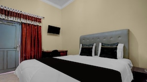 A hotel room with a bed, a desk, a chair, a television on the wall, and a door. - OYO 95262 Hotel Djatmiko Villa's Family  (Sumberagung)