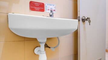 A bathroom with a white sink, a red warning sign, and a door with a keyhole.