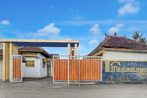 Ein umzäunter Villa-Komplex mit Ziegeldach, Holztor und Mauer mit einem Logo.