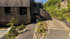 A modern building with a wooden facade, a stone staircase, and a garden area. - Luxury Apartment in Szczyrk | Mountain Views, Air Conditioning (Szczyrk)