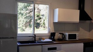 A compact kitchen with a refrigerator, microwave, coffee maker, and a window with a view of trees. - Beautiful, comfortable villa (Prunelli-di-Fiumorbo)