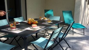 An outdoor dining area with a table set for four, surrounded by teal chairs, and a person holding a spoon. - Beautiful, comfortable villa (Prunelli-di-Fiumorbo)