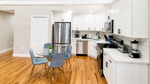 A modern kitchen with white cabinets, stainless steel appliances, and a dining area with a glass table and blue chairs. - Private 1BR Apt, 2BD 1BA, Sleeps 5, Clean & Reliable, Near NYC (Scotch Plains)