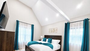 A bedroom with a wooden bed, teal curtains, a white wall, and a mounted TV. - Private 1BR Apt, 2BD 1BA, Sleeps 5, Clean & Reliable, Near NYC (Scotch Plains)