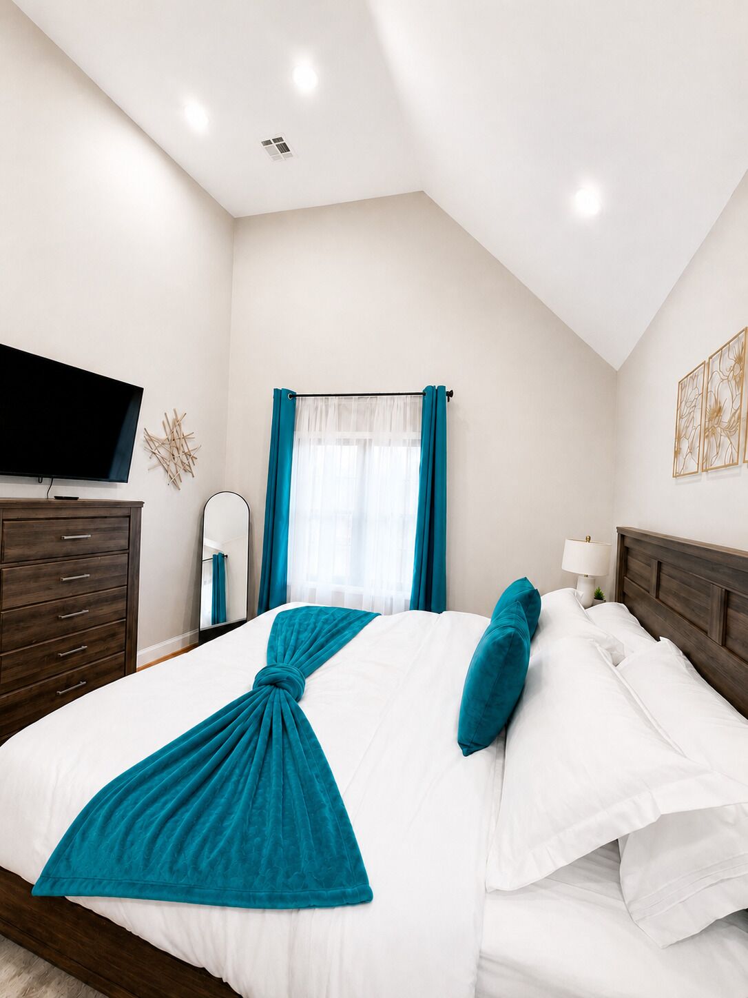 Habitación de hotel con cama, televisor, cómoda, ventana con cortinas y lámpara.