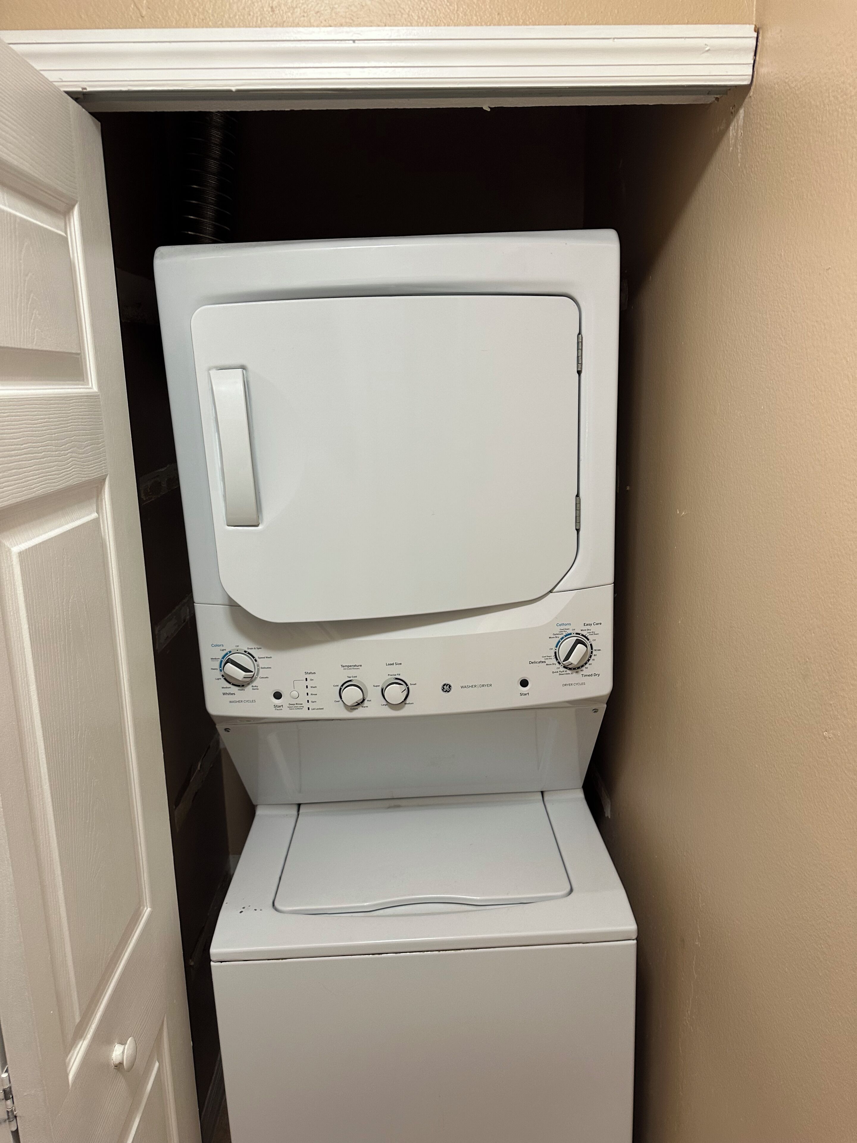 Une machine à laver et un sèche-linge blancs se trouvent dans une buanderie avec un mur beige et une porte blanche.