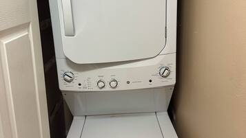 Une machine à laver et un sèche-linge blancs se trouvent dans une buanderie avec un mur beige et une porte blanche.