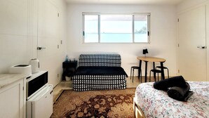 Ein Schlafzimmer mit Bett, einer Couch, einem kleinen Tisch mit Stühlen, einem Fenster mit Aussicht und einer Küchenzeile.