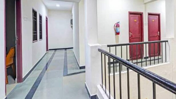 Un couloir doté d’un sol carrelé, d’une rambarde en métal et de portes rouges au fond.