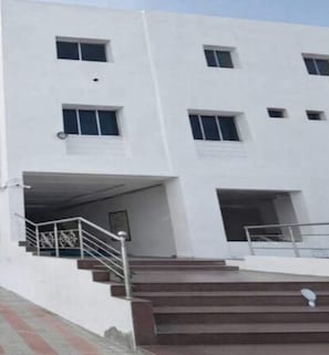 A multi-story building with a white facade, several windows, and a staircase leading to an entrance.