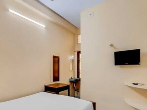 A hotel room with a bed, a small table, a TV mounted on the wall, and a bathroom with a sink and mirror.