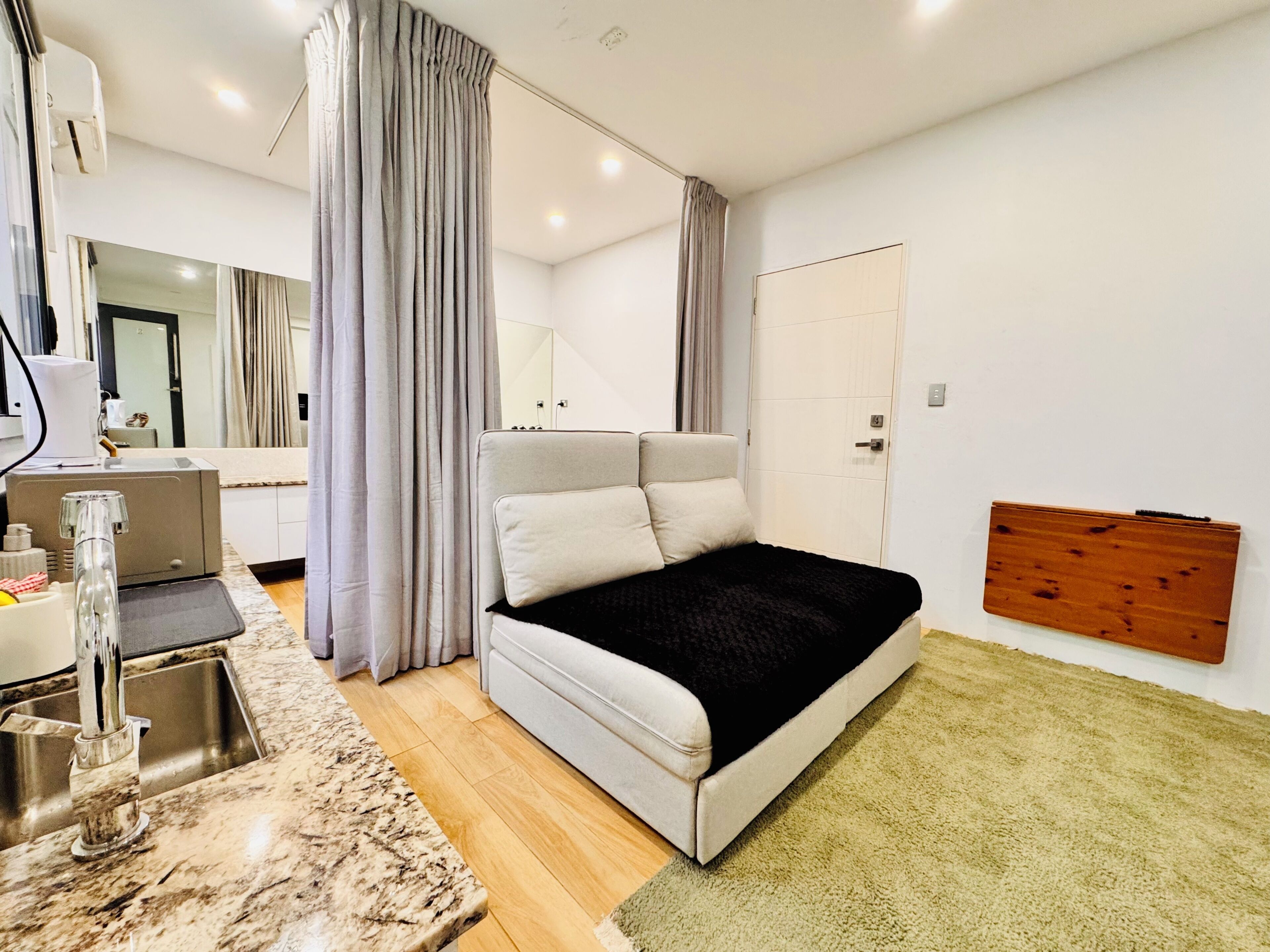 A modern bedroom with a bed, a sink, a mirror, and a wooden panel on the wall.