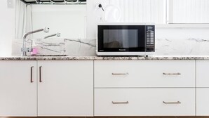 A kitchen with a white countertop, a microwave, a sink, and cabinets.