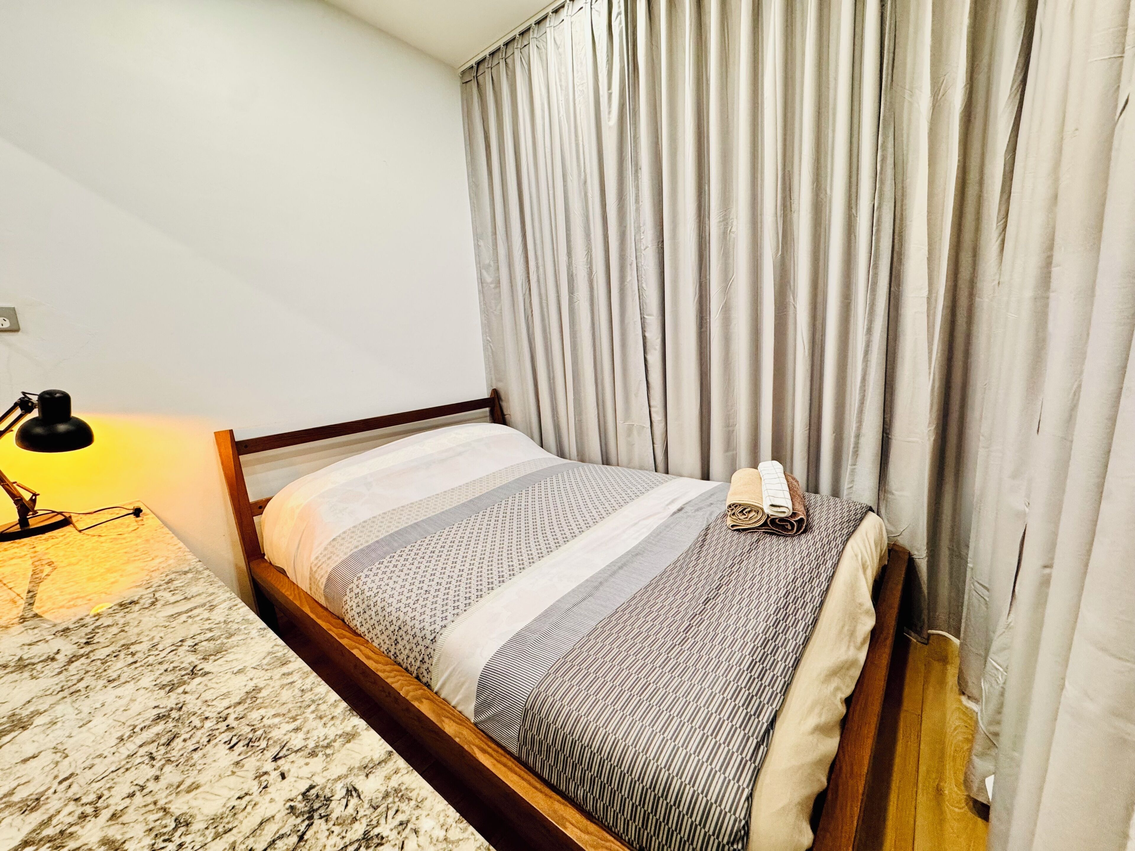 A single bed with a wooden frame, a bedside lamp, and a folded towel on the bed.