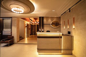 A reception desk with a circular logo, a modern light fixture, and a wall-mounted light panel. - HOTEL MURA BLISS (Indore)