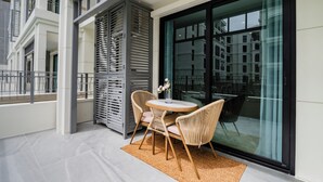 A balcony with a round table and chairs, a glass door, and a view of buildings. - Charming balcony studio in Title Legend (Choeng Thale)