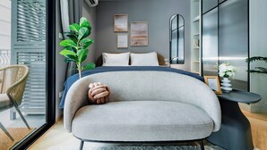 A modern bedroom with a bed, a chair, a plant, and artwork on the wall. - Charming balcony studio in Title Legend (Choeng Thale)