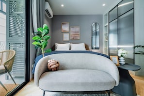 Ein modernes Schlafzimmer mit Bett, Sessel, Pflanze und Kunstwerk an der Wand.