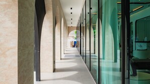 A corridor with glass walls, a tiled floor, and a series of columns. - Charming balcony studio in Title Legend (Choeng Thale)