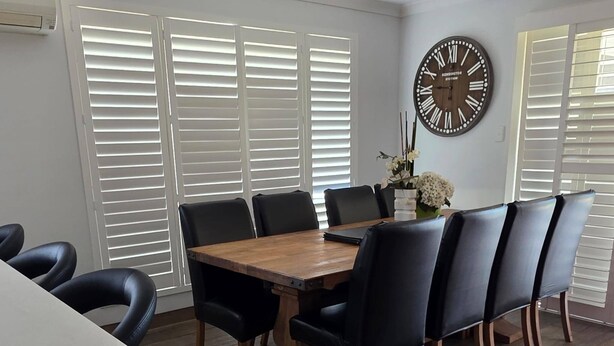 Uma área de refeições com mesa de madeira, cadeiras pretas e um relógio de parede grande.