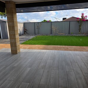 Eine Terrasse mit grau gekachelter Fläche, einer Steinpfeiler, einem kleinen Rasen und einem grauen Zaun.