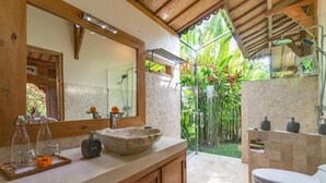 A bathroom with a large mirror, a stone basin, a toilet, and a shower area with a glass door. - Bali Sawah Indah  (Tampaksiring)