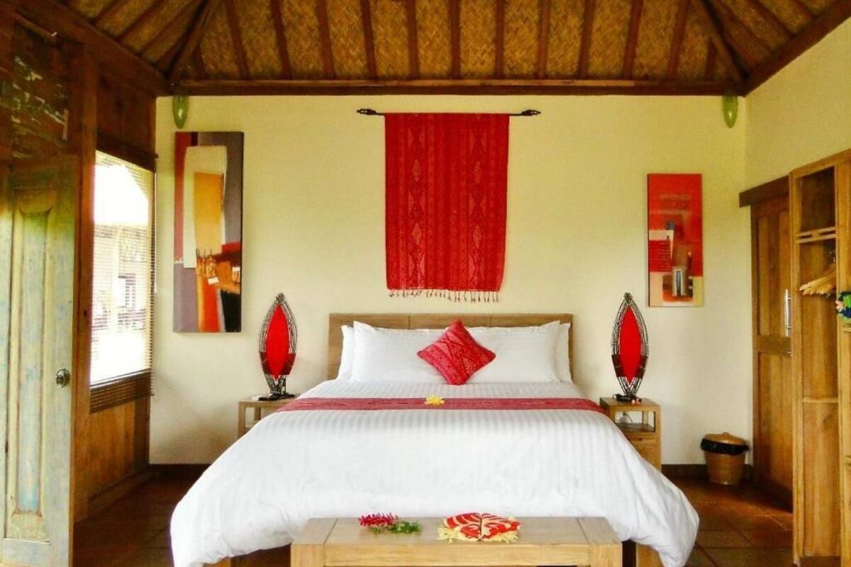 Una habitación con una cama, techo de madera, un tapiz rojo y una pequeña mesa con objetos decorativos.