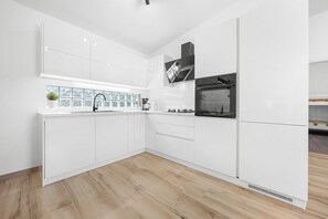 Eine moderne Küche mit weißen Schränken, einem Einbauofen und einem Fenster mit Blick auf Bäume.