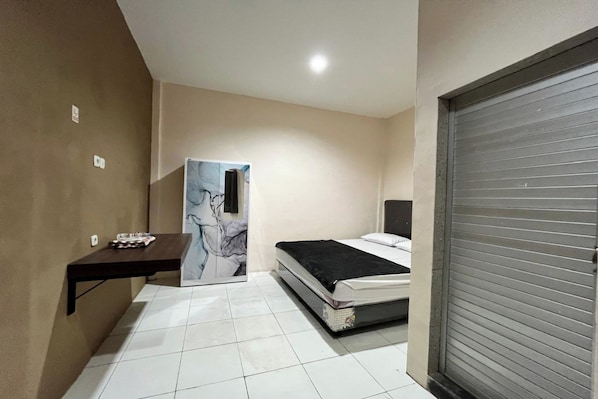 A bedroom with a bed, a desk, a chair, and a closed shutter door.